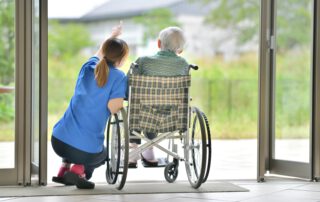 Pflegerin mit einem Senior im Rollstuhl auf der Terrasse.