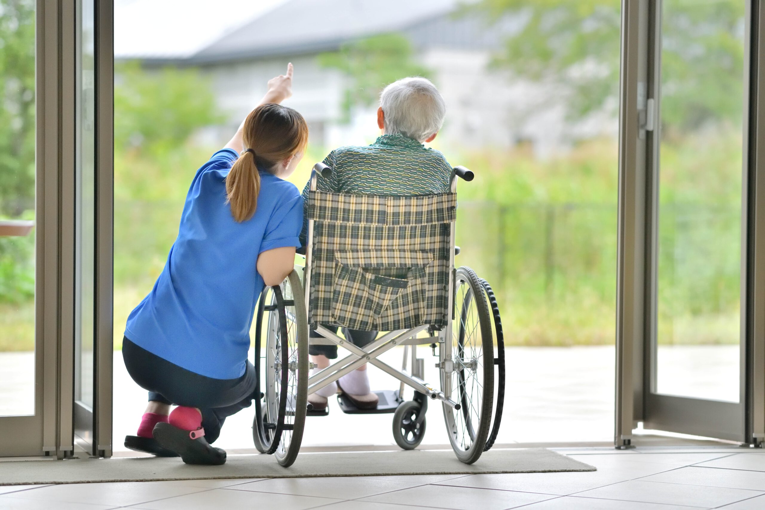 Pflegerin mit einem Senior im Rollstuhl auf der Terrasse.